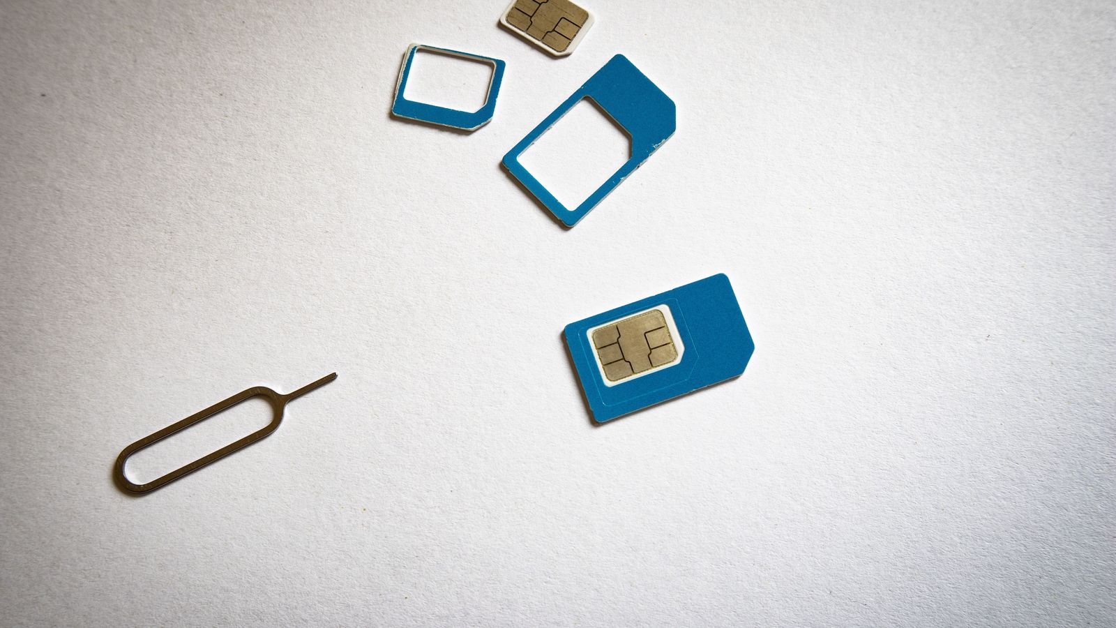Three SIM cards and a SIM ejector tool laid out on a white surface
